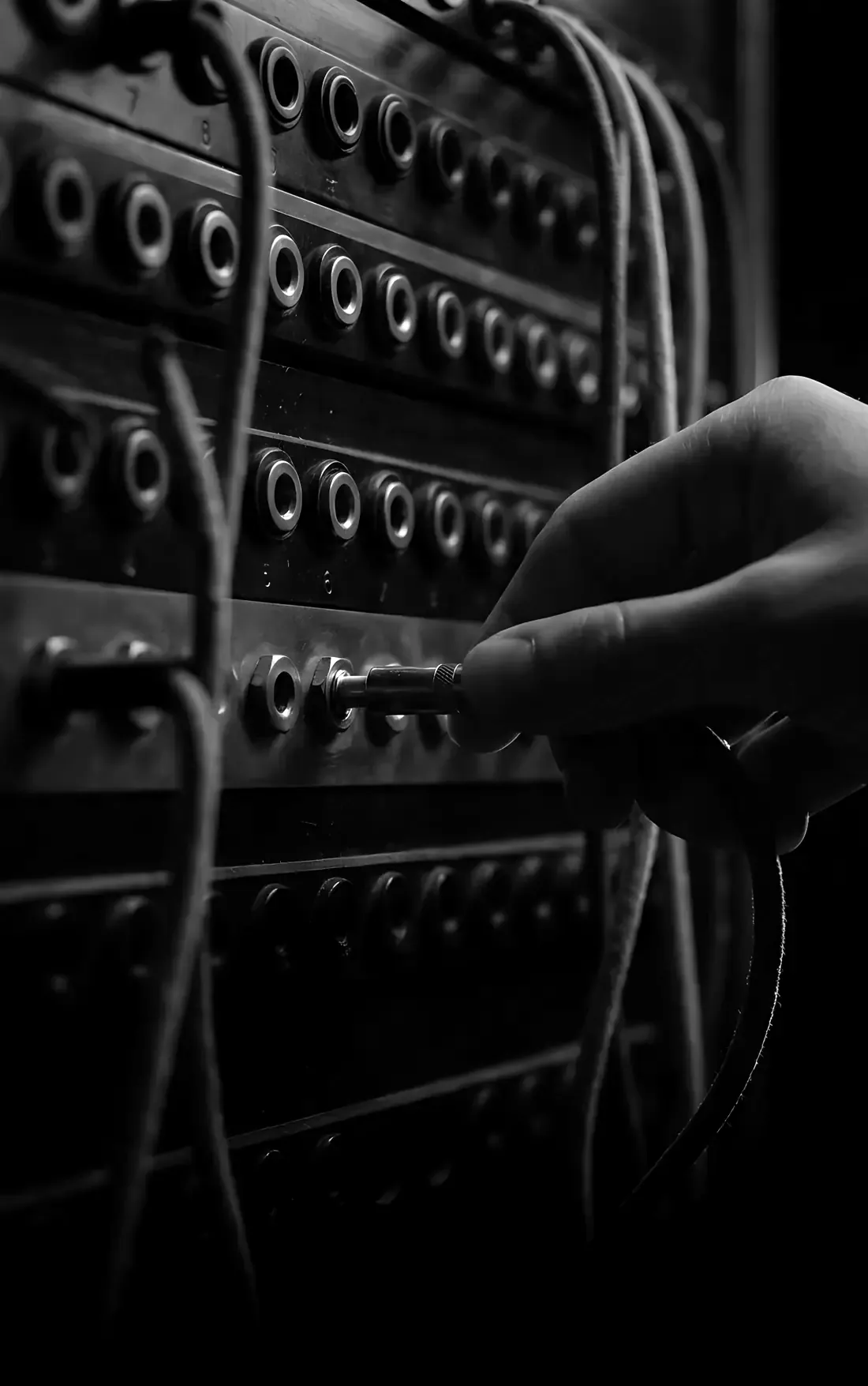 A hand plugging a patch cord into one socket of an old telephone switchboard